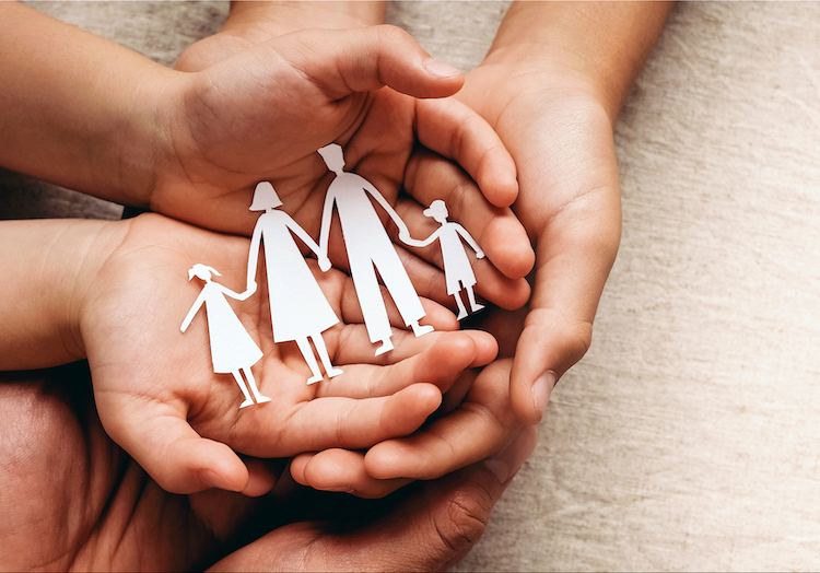 Photo of hands holding paper cut outs of a family