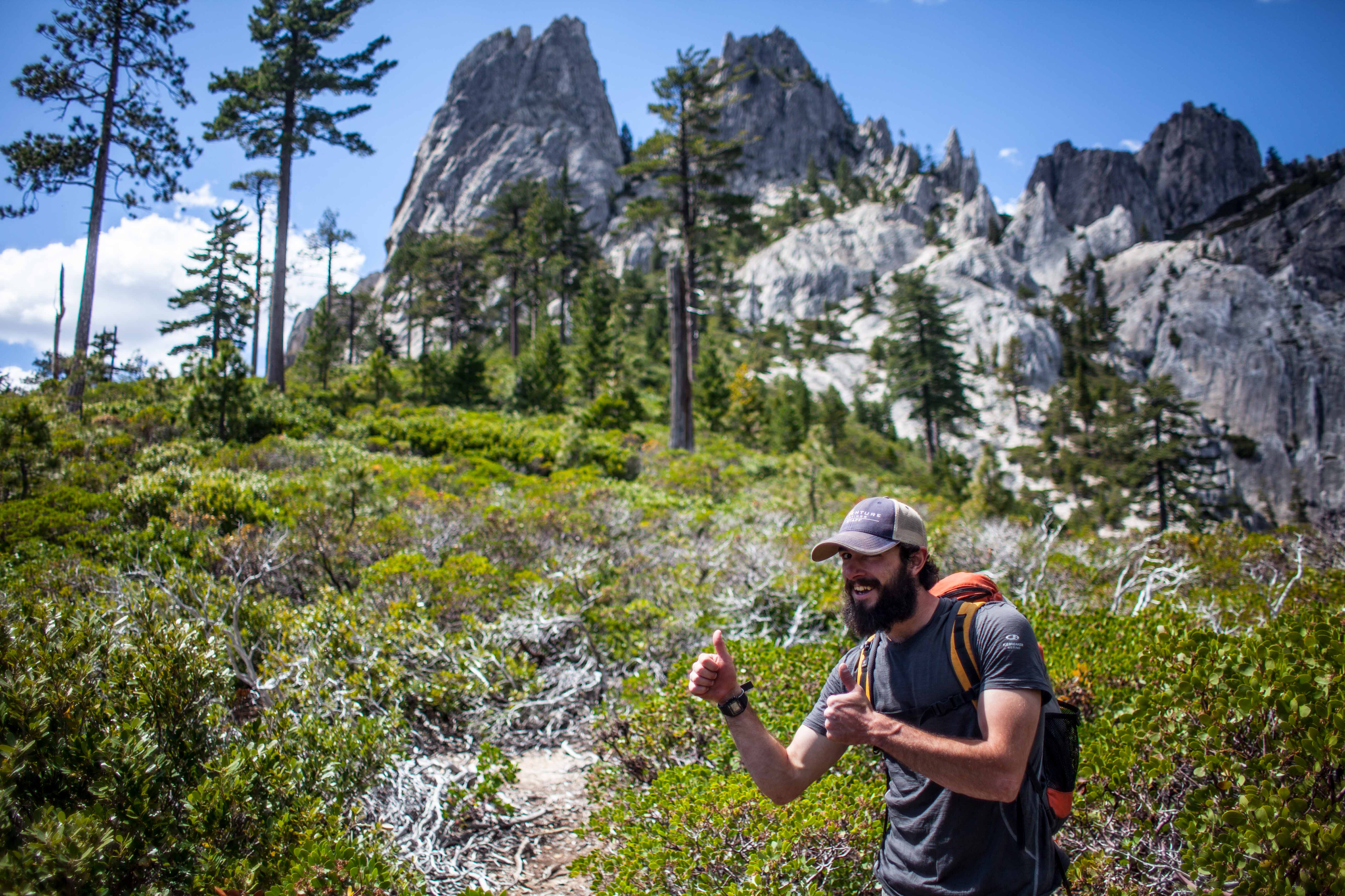 A young man giving a thumbs up against a backdrop of peaks and trees