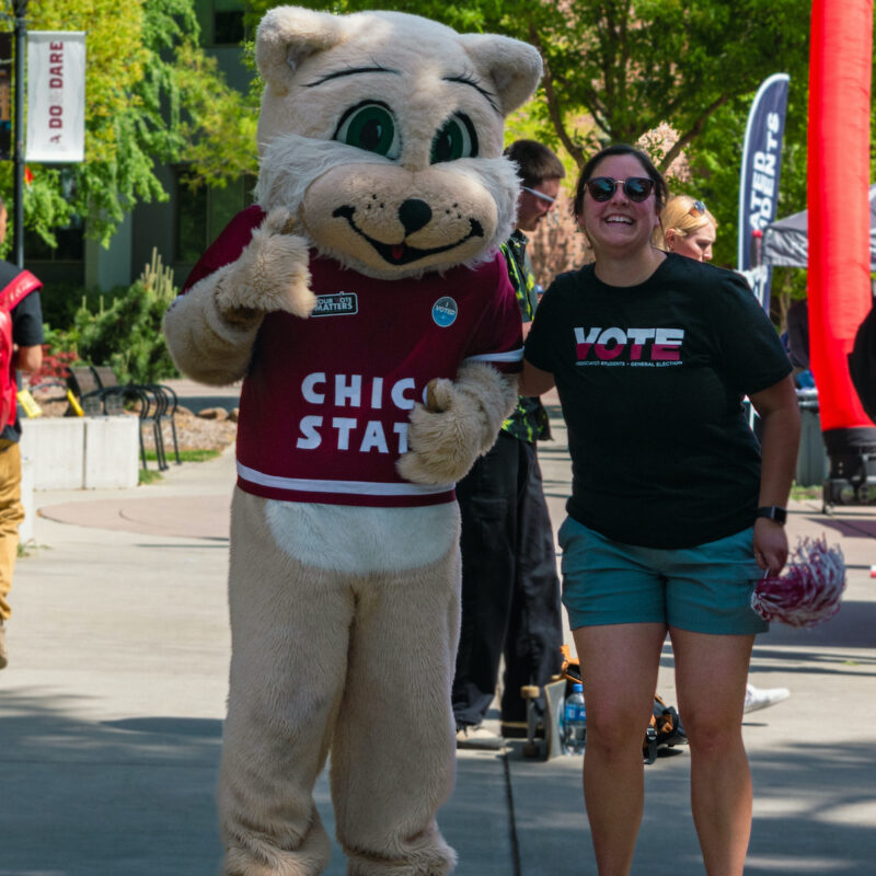 Willie the mascot and person wearing a VOTE shirt poses